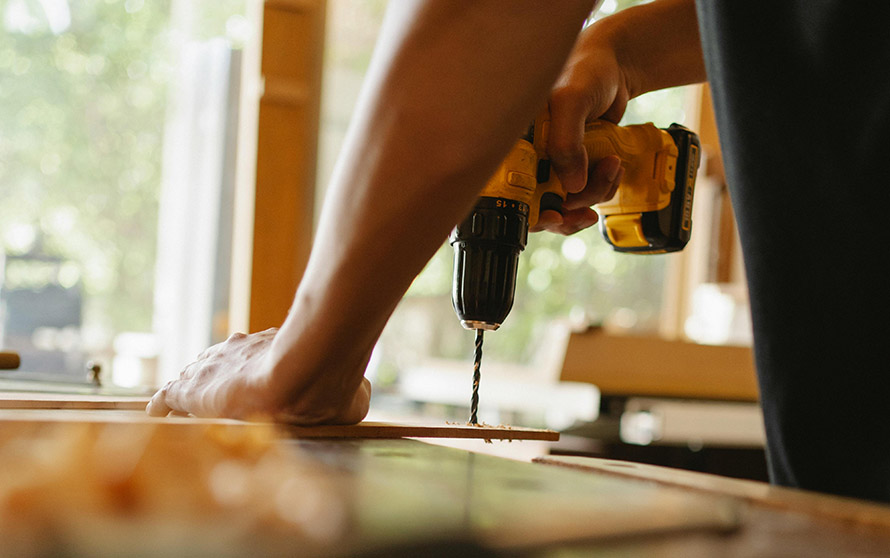 A Minneapolis handyman drills a wooden plank on a desk